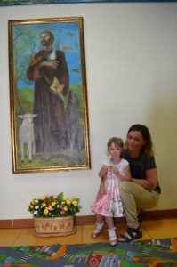 Dziewczynka z nauczycielką w holu z prawej strony obrazu przedstawiającego świętego Franciszka.