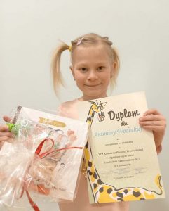 Dziewczynka trzyma w dłoniach dyplom oraz nagrodę.