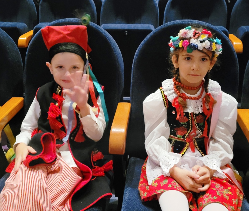 Zdjęcie przedstawia dwoje dzieci w strojach krakowskich z grupy ”Biedronek” siedzące na widowni w oczekiwaniu na występ.