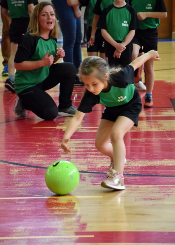 Dziewczynka podczas konkurencji sportowej toczy piłkę.