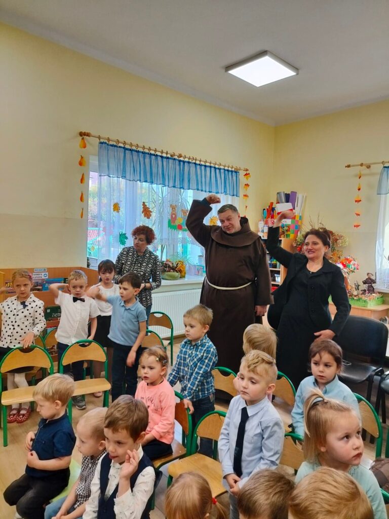 Dzieci, Pani Dyrektor i ojciec Lesław śpiewają piosenkę.