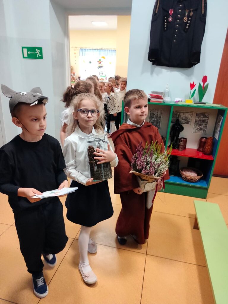 Dzieci z grupy Biedronek idą wręczyć ojcu Lesławowi prezent w podziękowaniu.