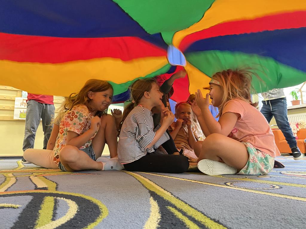 Dziewczynki siedzą na dywanie pod chustą animacyjną podczas zabawy.
