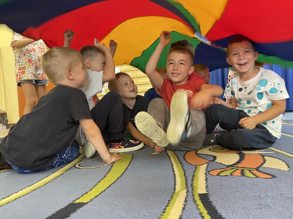 Chłopcy siedzą na dywanie pod chustą animacyjną podczas zabawy.