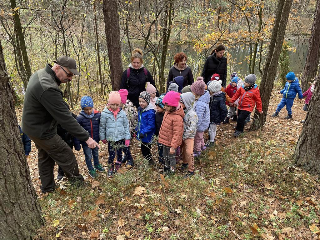 Dzieci spacerują po lesie z Panem leśniczym.